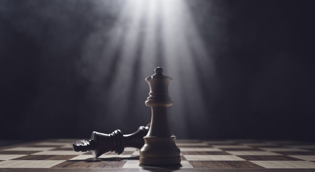 Chessboard with a white queen standing and a fallen black king under a spotlight, symbolizing victory